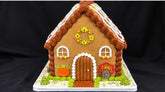 Harvest gingerbread house for Thanksgiving with a scalloped roof, fall leaves, a sunflower wreath, a pumpkin and a turkey by the front door
