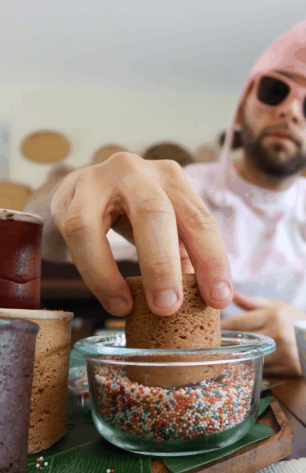 Hand dipping a Dirty Cookie cookie shot into a bowl of rainbow sprinkles