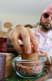 Hand dipping a Dirty Cookie cookie shot into a bowl of rainbow sprinkles